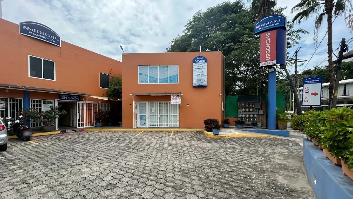 Entrada de Clínica Mediciel vista desde el estacionamiento, con el letrero de servicios y el poste de Urgencias.