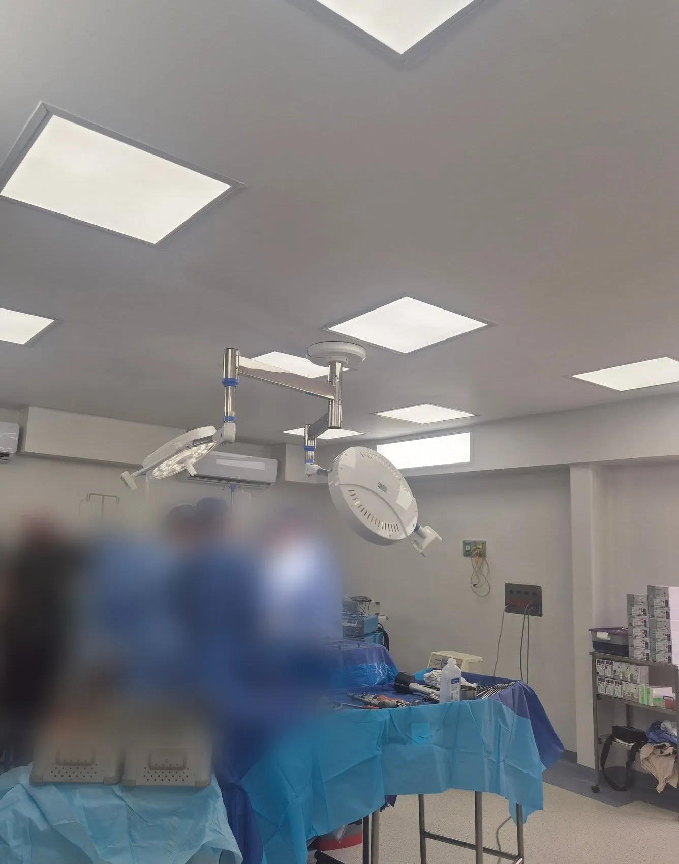 Quirófano de la clínica con lámparas quirúrgicas en el techo; el equipo médico aparece difuminado.